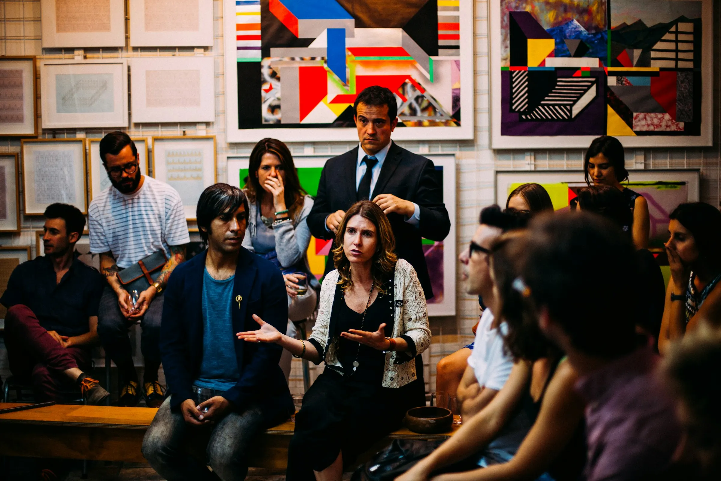 Grupo sentado em roda conversa em uma sala com quadros coloridos na parede.